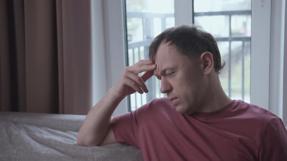 Portrait of Irritated Man on Sofa Window Background alt