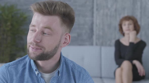 Portrait of the Young Man in Blue Shirt Sitting in the Foreground. The Blurred Figure of Mature Lady alt