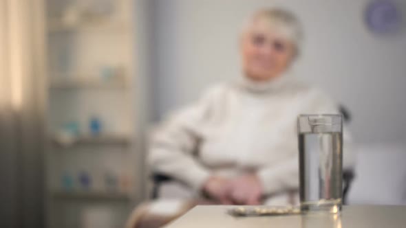 Depressed Old Woman Sitting in Wheelchair and Looking at Medicines, Diagnosis alt