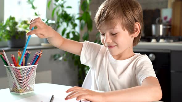 Cute Smiling Boy Draws with Colored Pencils at Home at the Table Happy Baby alt