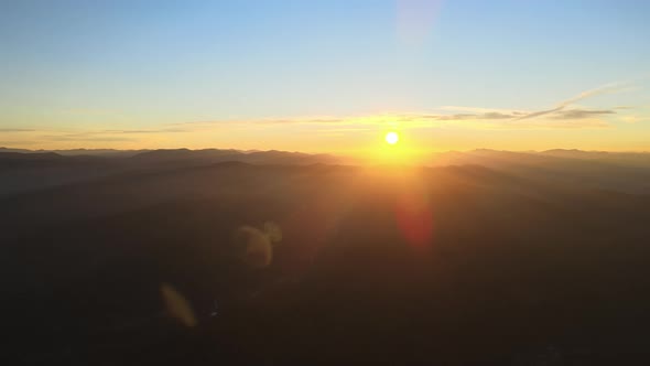 Aerial View of Dark Mountain Hills with Bright Sunrays of Setting Sun at Sunset alt