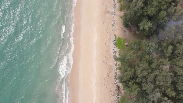 Top down aerial view and fly over beach near resort or village with green color of water