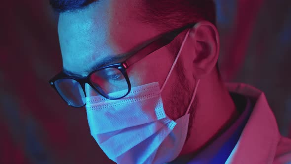 Portrait of young handsom doctor looking at camera with protective mask and eyeglasses on his face. alt