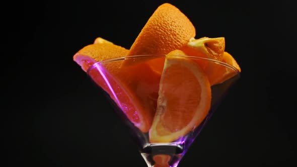 Oranges In A Martini Glass Rotate On A Black Background In A Purple Hue In The Center