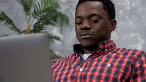 Smiling Adult African American Man Sitting on Couch Works for Laptop Typing Text alt