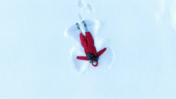Girl in a Red Down Coat Making a Snow Angel. Aerial, Camera Rises Up in a Spiral, Top View alt