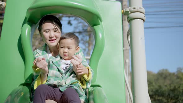happiness cheerful asian male child and his mother playing green slider toy at playground alt