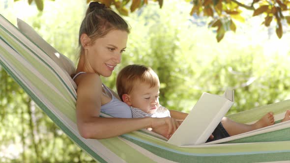 smiling happy mother reads a book hugging and cuddling her little baby son, relaxing lying together