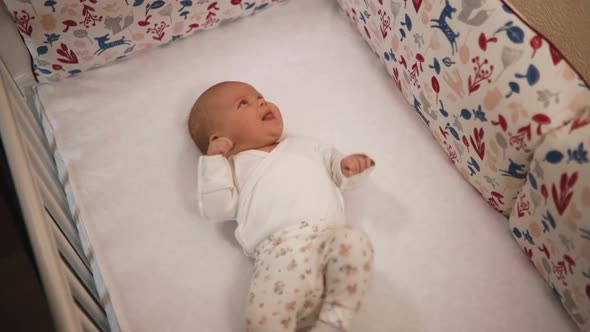 Funny Female Toddler Smiles and Moves Hands in Crib at Home alt