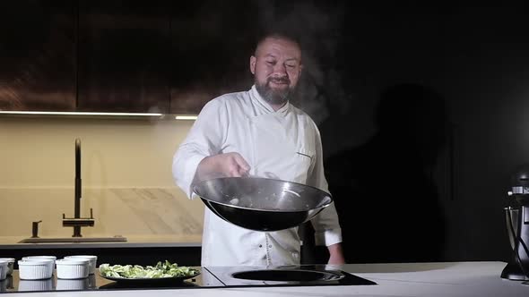 Cook man throws food in wok pan to mix all  ingredients.