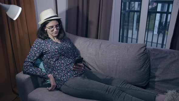 Girl Student Reads Messages in Her Mobile Phone While Sitting on the Couch in the Evening Copyspace alt