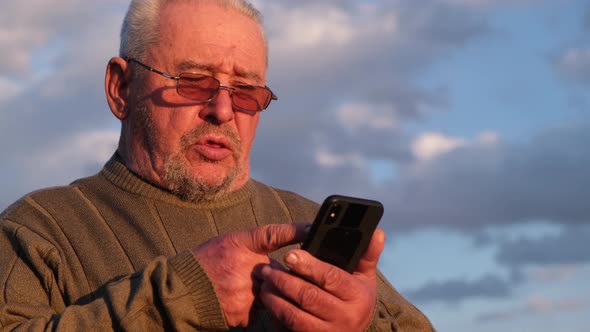 Senior Man Looking at Smartphone on Blue Sky Background alt