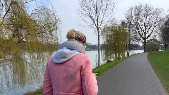 Tracking shot of fashionable young girl checking mobile phone during walk on bank of river during be alt