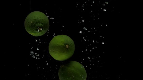 Slow Motion Three Lime Falling Into Transparent Water on Black Background alt