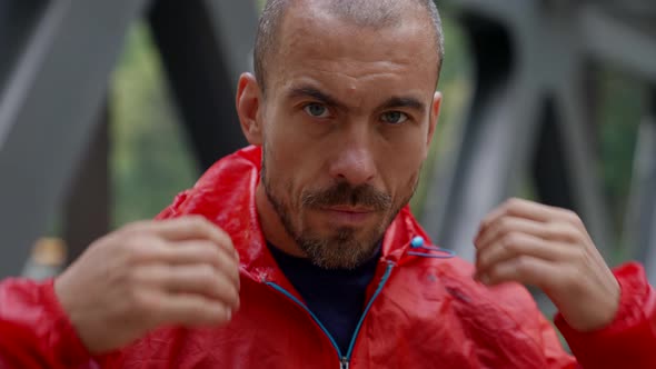 Serious Man is Putting on Head Red Hood and Kneading Hands Looking at Camera alt