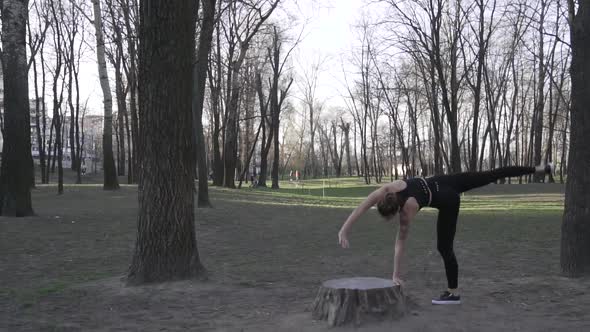 A Young Caucasian Woman Does a Handstand in a Wooded Area, Leaning Her Hands on a Stump Tree alt