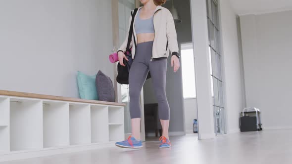Caucasian female ballet dancer entering a studio, smiling and sitting on a bench alt