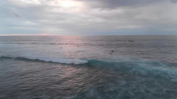 Aerial flyover view of waves crashing during sunset with people swimming in the sea in Bali