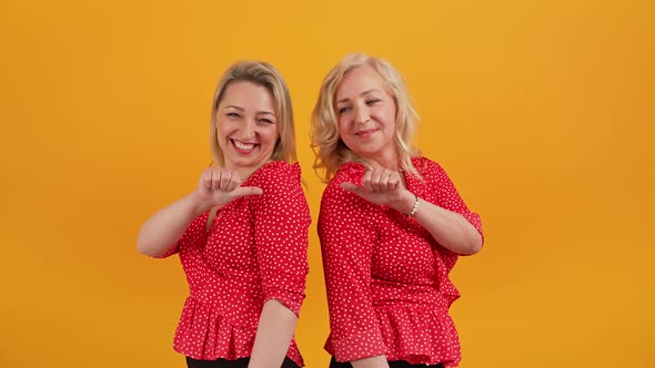 Two Attractive Cute Middleaged Women Standing Back to Back Pointing at Each Other with Their Thumbs alt