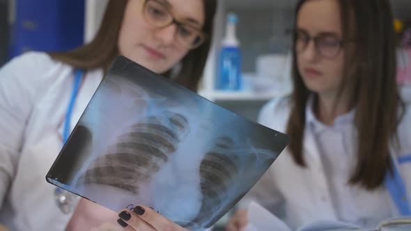 Two Female Doctor with Glasses Holds Up Series of Xray Picture of Breast