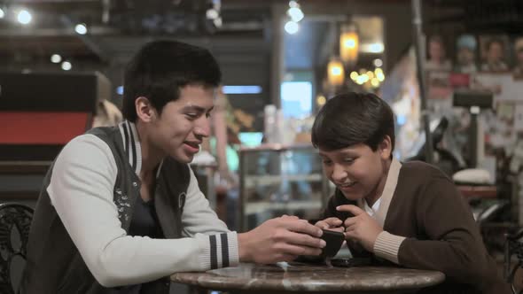 Two brothers with smartphone in cafe alt