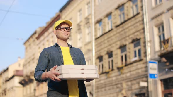 A Young Happy Delivery Man is Going and Holding Three Pizza Boxes alt