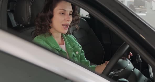 Young Beautiful Girl Chooses New Car at Car Dealership. The Woman Is Happy, Smiling and Rejoicing in alt