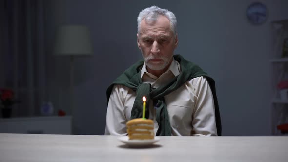 Depressed Senior Man Looking at Birthday Cake, Celebrating Holiday Alone at Home alt