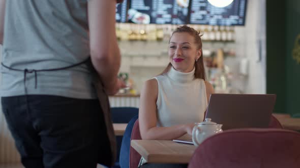 Attractive Longhaired Girl Works with Laptop in Cafe Waiter Brings Her Cake