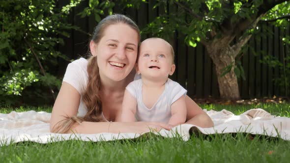Cheerful Smiling Mother Lying Next to Baby Son on Grass and Hugging Him alt