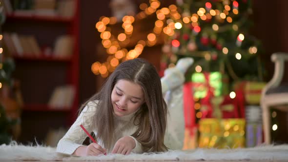 cute little girl lies on the floor and writes a letter to Santa Claus