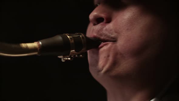 Man Blows Into the Mouthpiece of a Saxophone with Mouth in Darkness Closeup alt