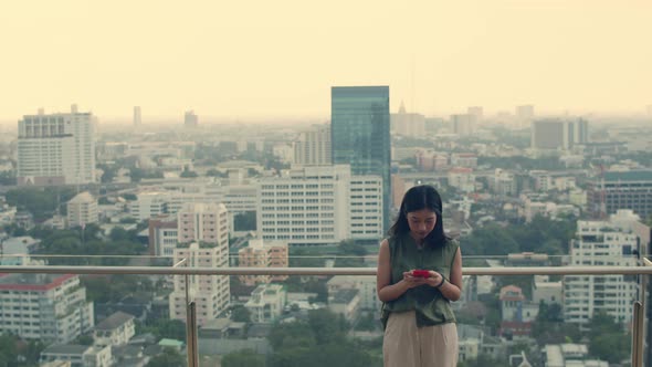 Asian woman using smartphone while standing on the rooftop building.