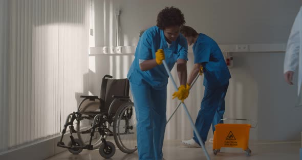 Diverse Janitors Washing Floor in Hospital Room with Empty Wheelchair alt