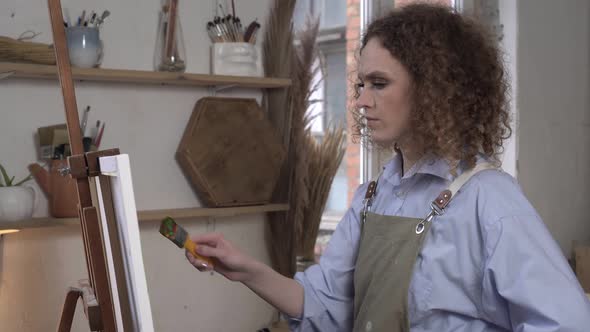 Serious Woman Artist Paints a Picture in a Studio with Concentration alt