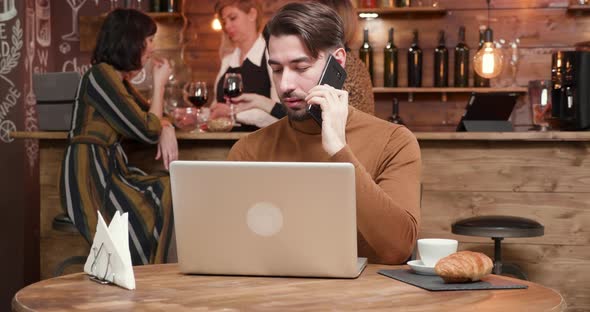 A Handsome Young Businessman Talking on His Phone While Working in a Bar alt