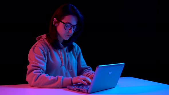 Young Woman with a Laptop. A Woman Is Using a Laptop. Blue and Red Light Falls on a Woman on a Black alt