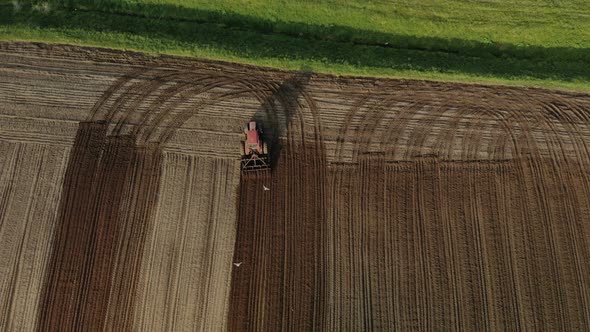 Red Tractor with Dual Wheels Doing the Processing Brown Soil with a Disc Cultivator alt