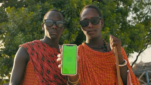 Extremely Happy Masai Tribe Men Showing Green Screen on Smartphone and Making Thumb Up Sign