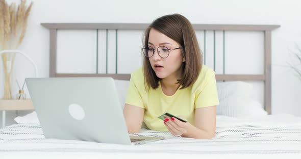 Young Beautiful Woman is Lying on the Bed in Front of a Laptop