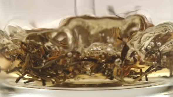 Water fall into a glass cup and tea leaves twist under a water