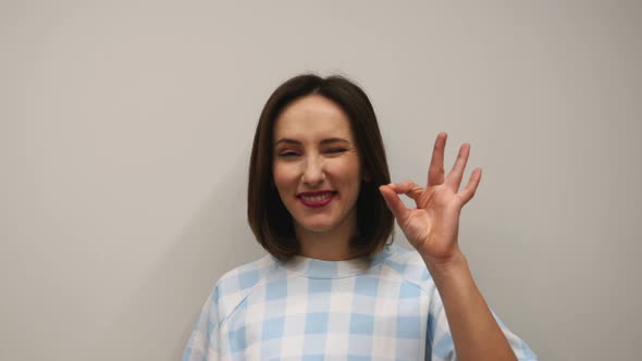 Female doing ok gesture in studio against white wall. alt