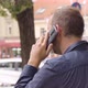 A Caucasian Man Talks on a Smartphone in an Urban Area  Rear Closeup  a Colorful Street - VideoHive Item for Sale