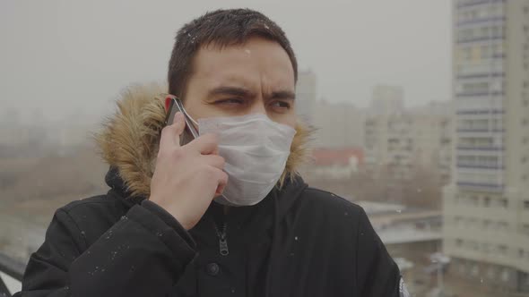 A Masked Man Speaks on His Phone in the Background of the City