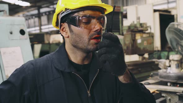 Factory Worker Talking on Portable Radio While Inspecting Machinery Parts alt