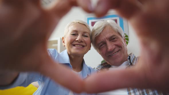 Senior Beautiful Coupled Doing Heart Shape with Hand and Fingers in Living Room alt