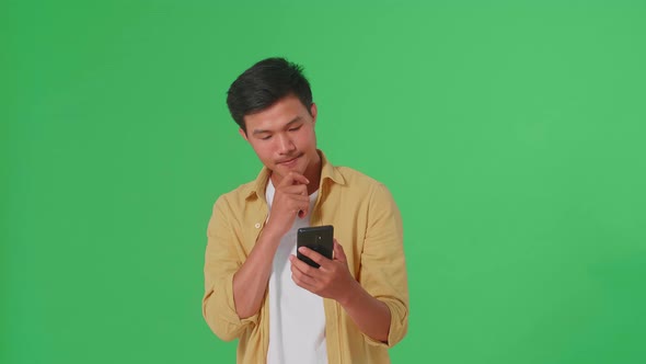 Young Asian Man Use Mobile Phone And Thinking About Something In Green Screen Studio alt