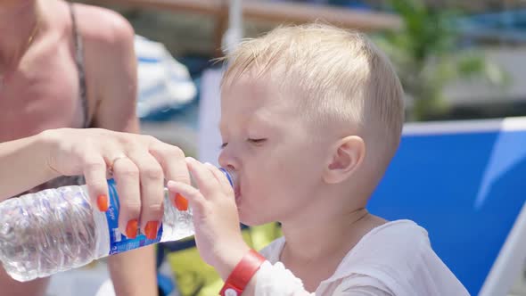 Mom Give Water To a Little Son on the Beach on a Sunny Summer Day. alt