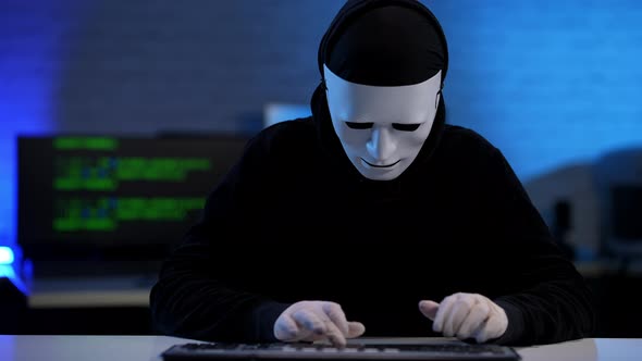 Concentrated Hacker Typing on Keyboard Raising Masked Face and Pointing at Camera alt