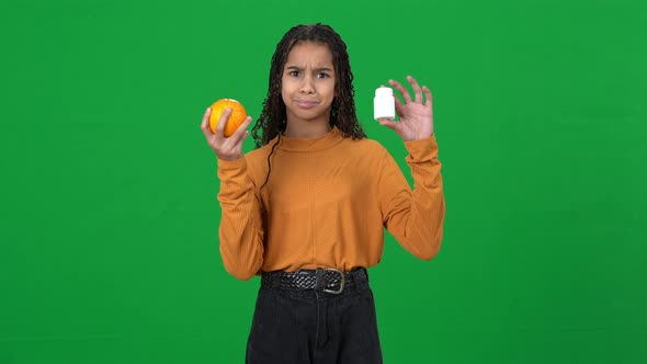 Unsure African American Teen Girl on Green Screen Holding Drugs and Orange Shrugging Shoulders alt